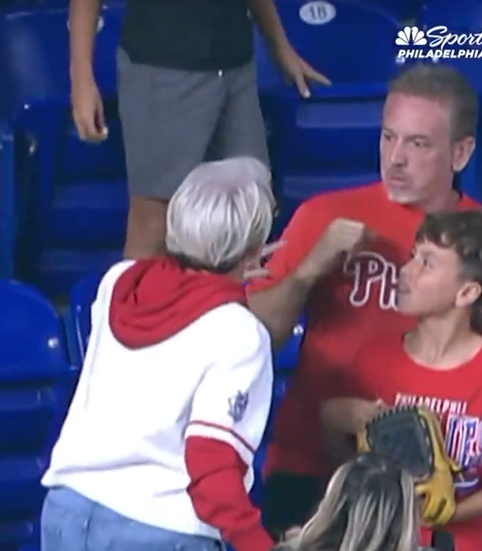 A woman in a white jacket confronts a Dodgers fan sitting with a young fan holding a baseball glove.