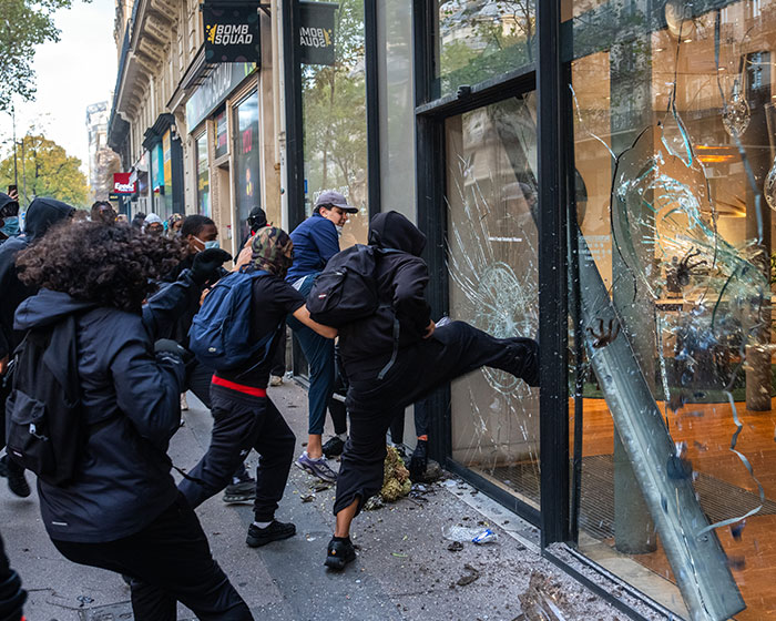 Rioters kicking and smashing a glass storefront window during the France riots