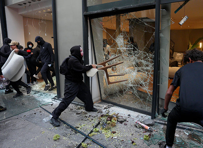 Masked looters in France breaking store glass windows with a chair during civil unrest.
