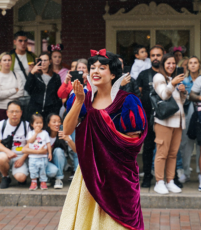 Disney World guest and performer dressed as Snow White waving to a crowd of visitors. Disney World guest and performer dressed as Snow White waving to a crowd of visitors.