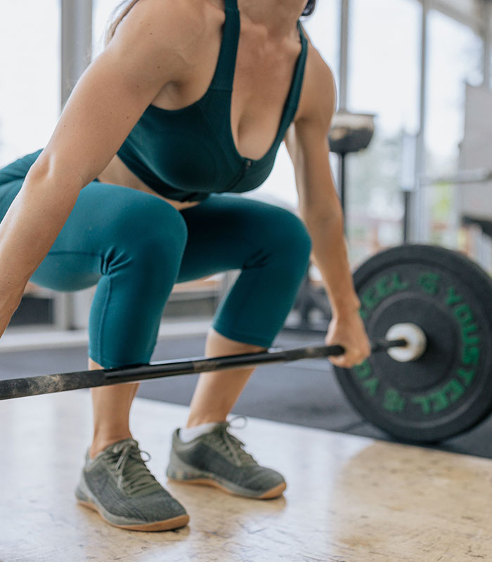 Female weightlifter preparing for a lift with a barbell in a gym setting. Female weightlifter preparing for a lift with a barbell in a gym setting.