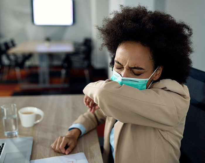 A woman wearing a protective mask coughing into her elbow, concerned about rising cancer rates. A woman wearing a protective mask coughing into her elbow, concerned about rising cancer rates.