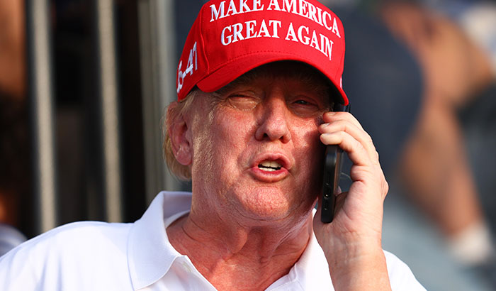 Donald Trump wearing a red hat while making a call on a mobile phone during a public appearance.