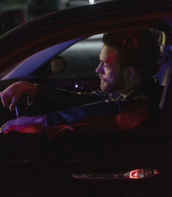 A man sitting in a car under neon lights reflecting on his marriage sacrifices