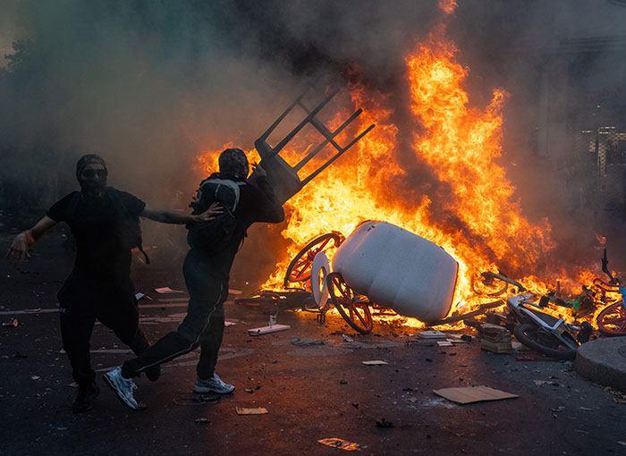 Rioters throwing items into a large street fire amid unrest and looters in France.