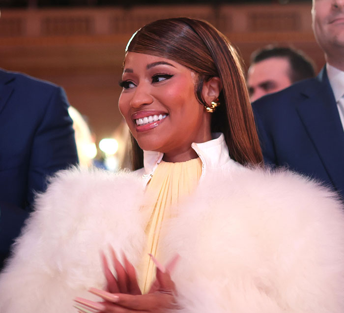 Nicki Minaj smiling in a white faux fur coat during a public appearance at a Trump Rally.