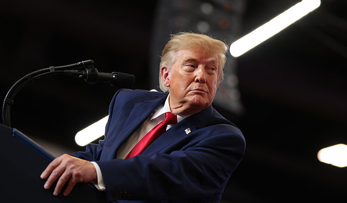 Donald Trump speaking at a podium during an event discussing news related to Trump Mobile.