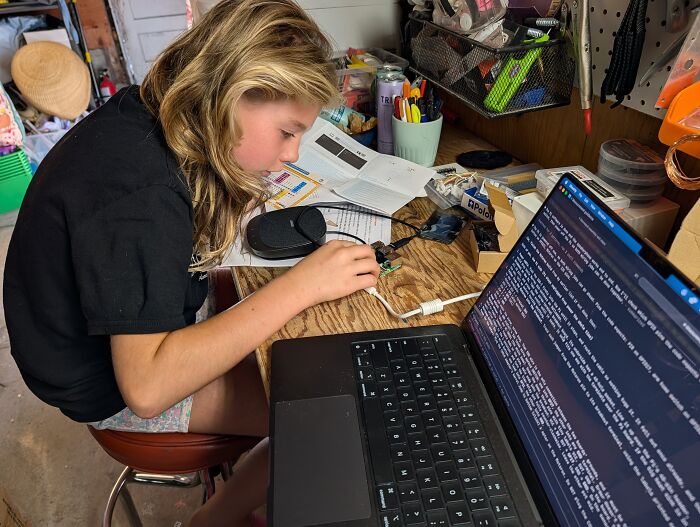 A young girl coding on a laptop next to a tiny computer circuit board. A young girl coding on a laptop next to a tiny computer circuit board.