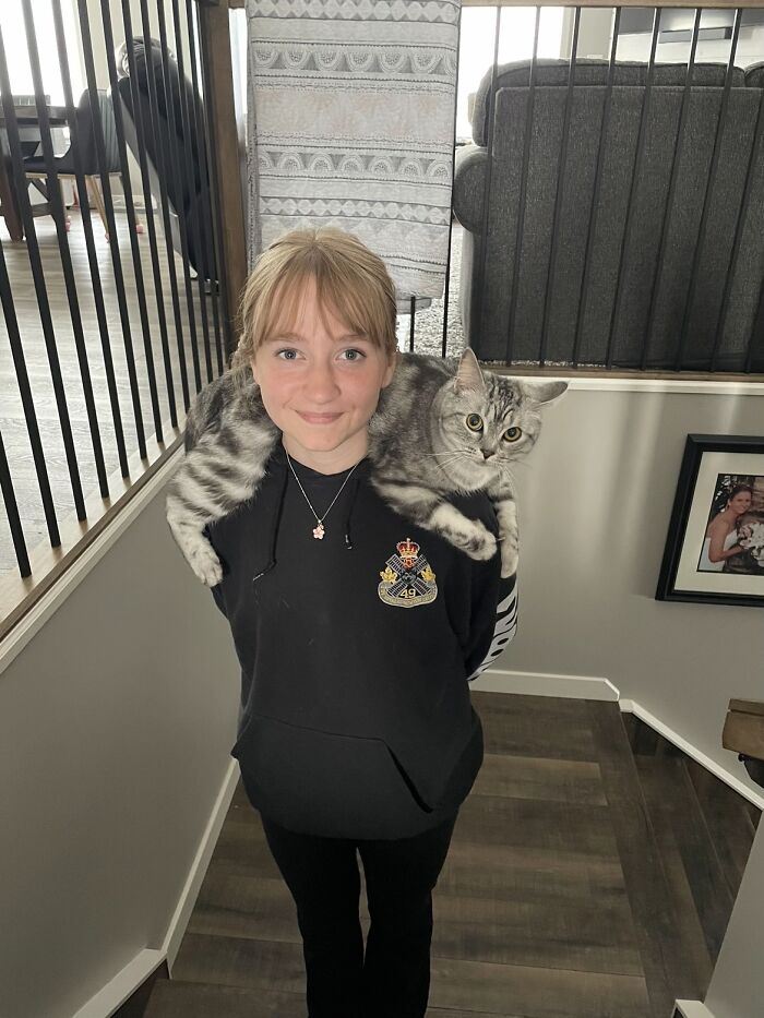 A girl smiling with her tabby cat draped over her shoulders, sharing life stories with pets