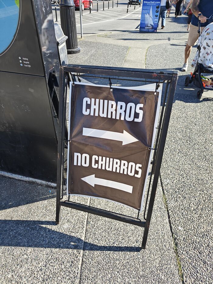 An A-frame sign pointing left and right with absurd signs for Churros and No Churros.