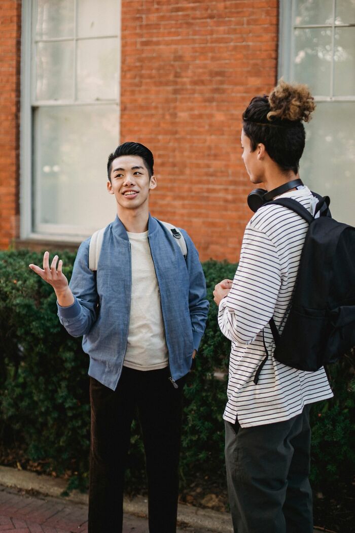Two young men casually chatting outdoors against a brick wall