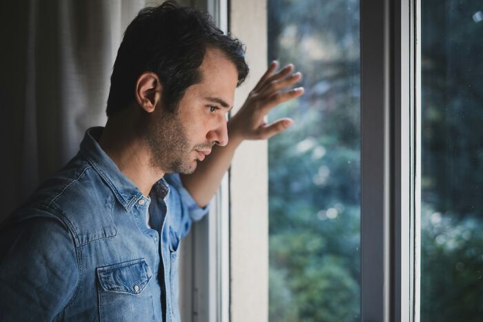 Pensive man looking out a window thoughtfully during difficult moments before deciding to choose divorce.