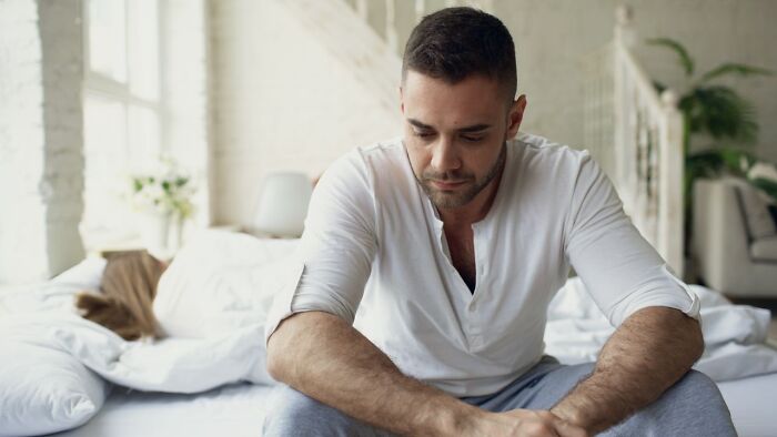 A thoughtful man sitting on a bed reflecting on his decision regarding divorce
