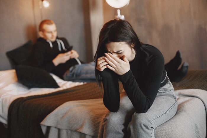 Distressed woman crying on a bed while her partner ignores her, a moment that makes one choose divorce.