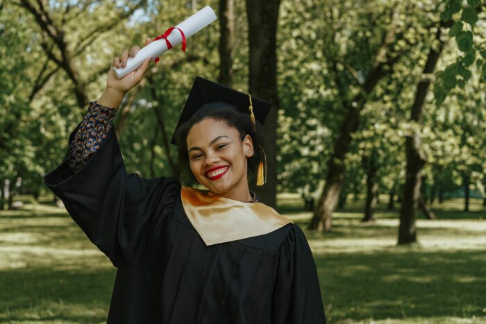 A happy student in graduation cap and gown holding a diploma outdoors. A happy student in graduation cap and gown holding a diploma outdoors.
