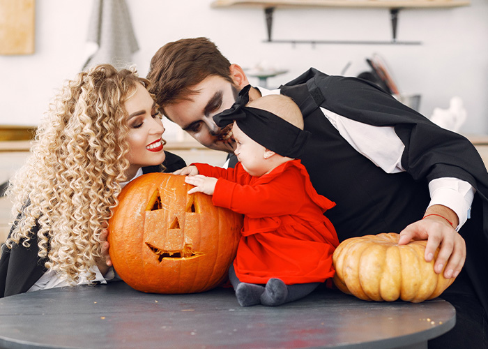 Parents dressed in costumes with their baby and a carved Halloween pumpkin
