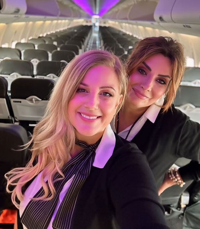 An air hostess and her colleague smile together inside a commercial airplane cabin.
