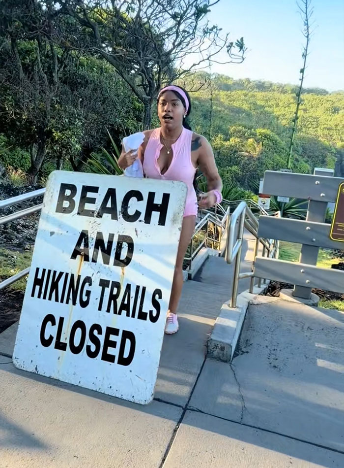 A tourist stands next to a Beach and hiking trails closed sign
