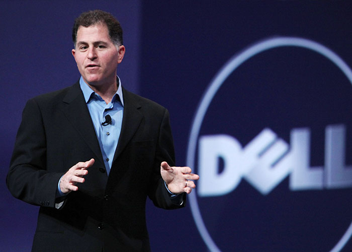 Dell CEO Michael Dell speaking on stage in front of a blue Dell logo backdrop.