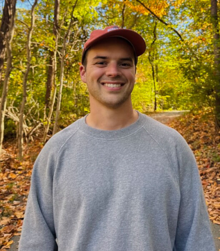 A Christian man smiling outdoors in autumn, wearing a cap and grey sweater.