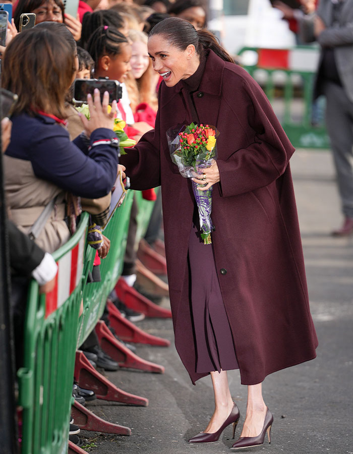 Meghan Markle greeting crowds while holding a bouquet of flowers during a public appearance.