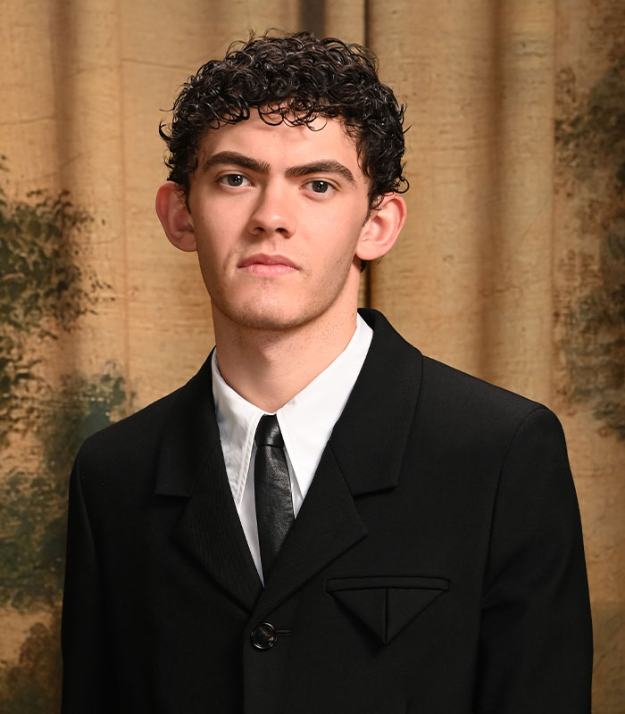Hollywood star Joe Locke wearing a black suit and tie posing indoors.