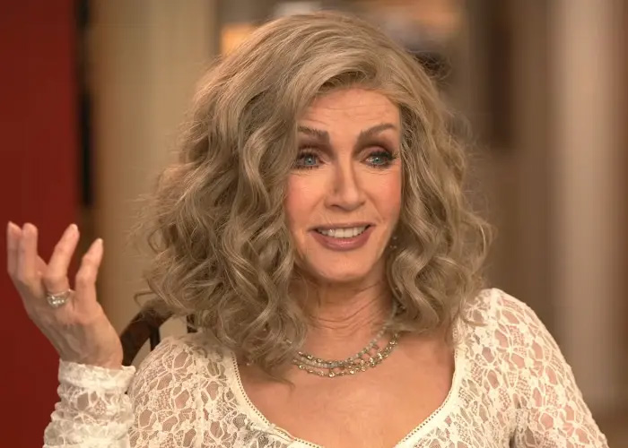 Knots Landing star Donna Mills gesturing while speaking in a white lace top during an interview.