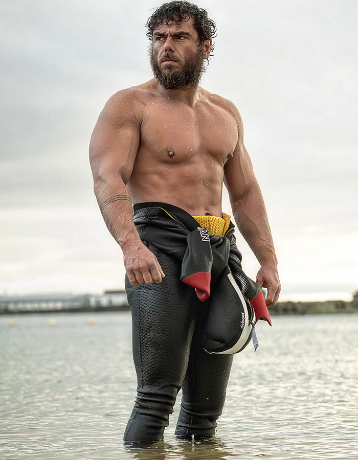 Extreme swimmer standing in shallow ocean water wearing a partially unzipped wetsuit. Extreme swimmer standing in shallow ocean water wearing a partially unzipped wetsuit.