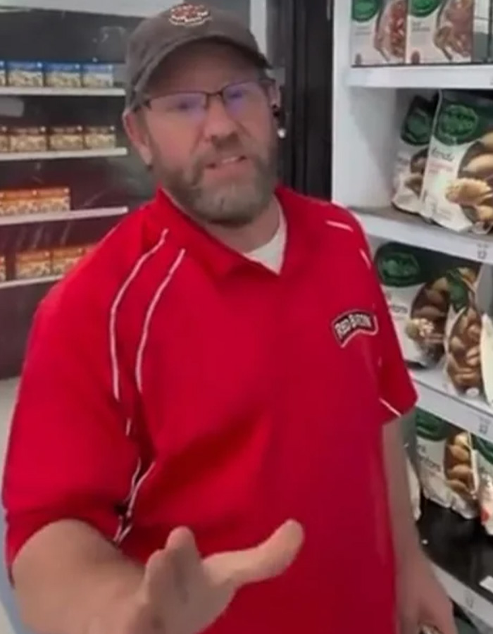 A store employee in a red shirt gestures frustratedly at an Instagram prankster filming him. A store employee in a red shirt gestures frustratedly at an Instagram prankster filming him.