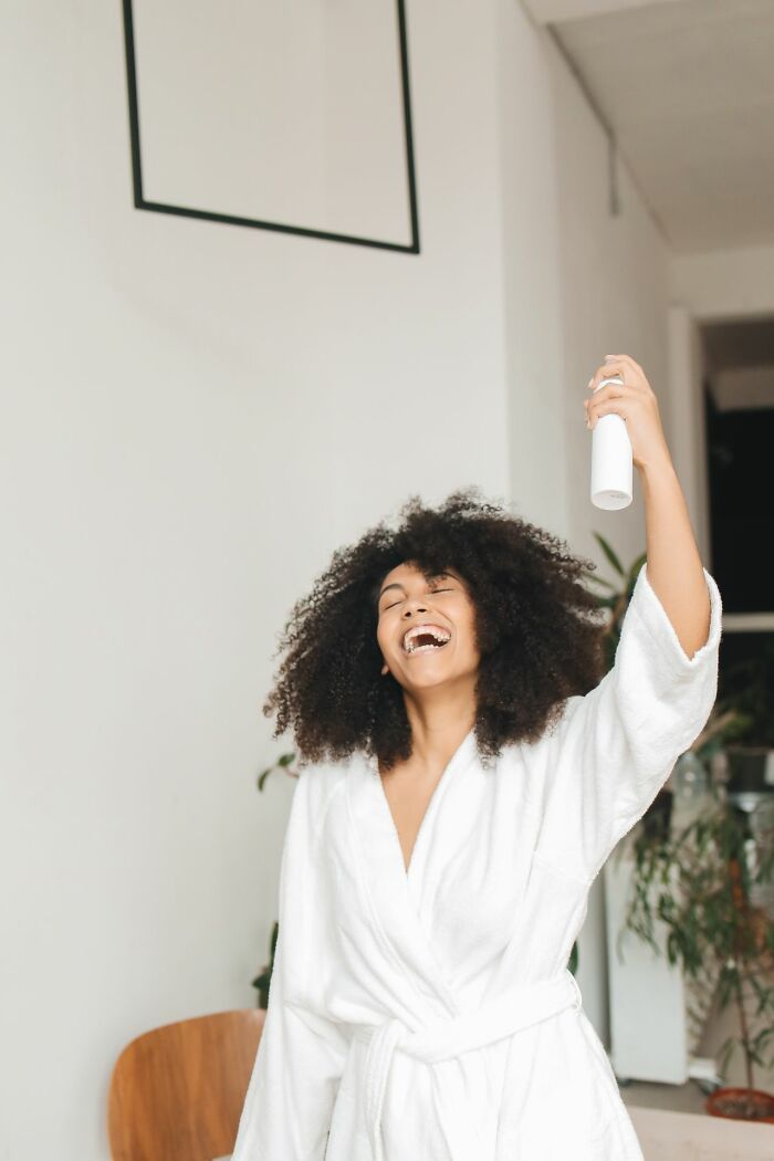 Woman in bathrobe happily spraying deodorant casually admitting disturbing things
