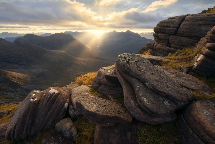 Sun rays streaming through mountain peaks over rocky terrain, captured in natural landscape photography.