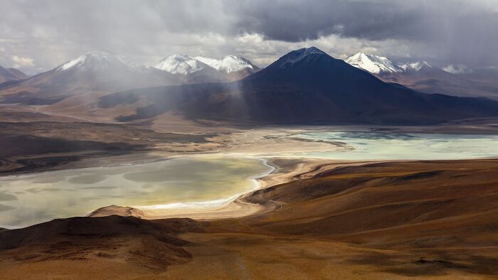 Dramatic mountain landscape photography featuring snow-capped peaks and a desert valley lake.