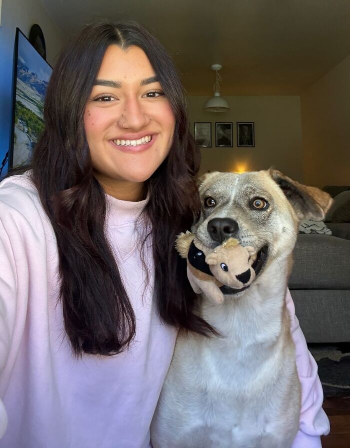 Woman smiling next to a happy rescue dog holding a plush toy in its mouth.