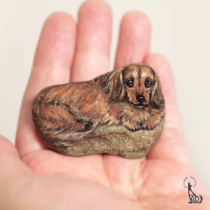 Hand holding stone painted as detailed brown dog by Japanese artist