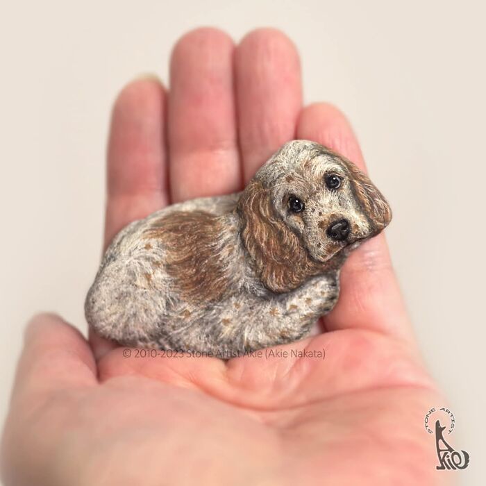 Hand holding stone painted as detailed speckled dog by Japanese artist