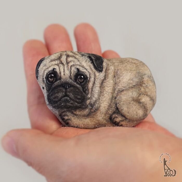 Hand holding stone painted as detailed pug dog by Japanese artist