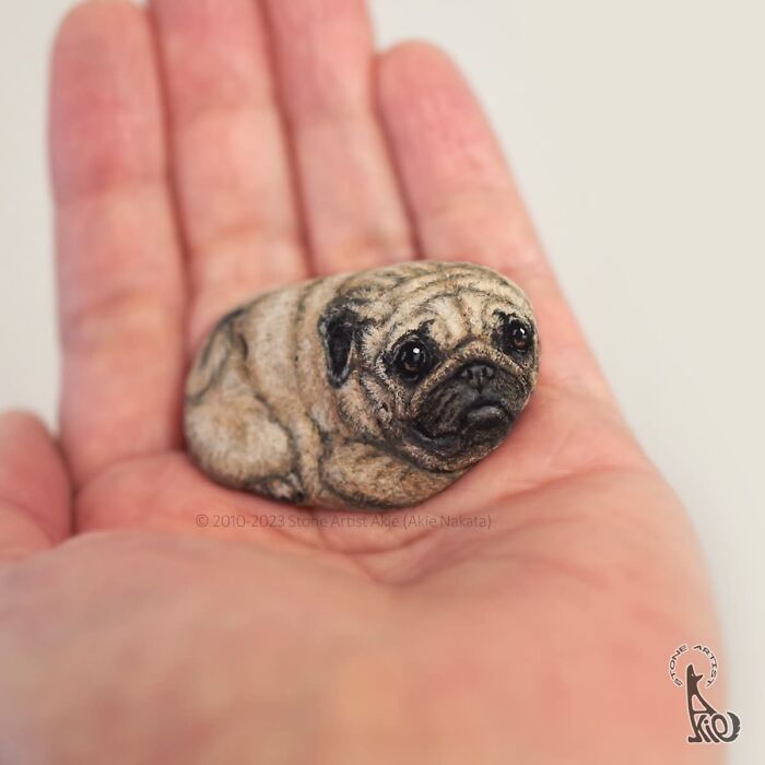 Hand holding stone painted as detailed pug dog by Japanese artist
