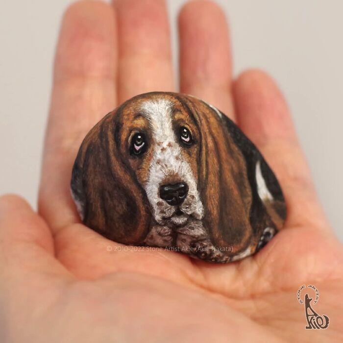 Realistic dog face painted on stone held in a hand by Japanese artist