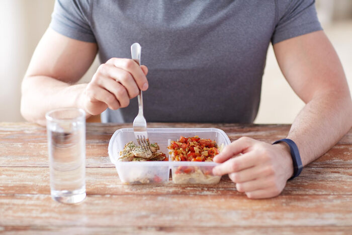 Man eating chicken lunch with odd sides at wooden table with glass of water Man eating chicken lunch with odd sides at wooden table with glass of water