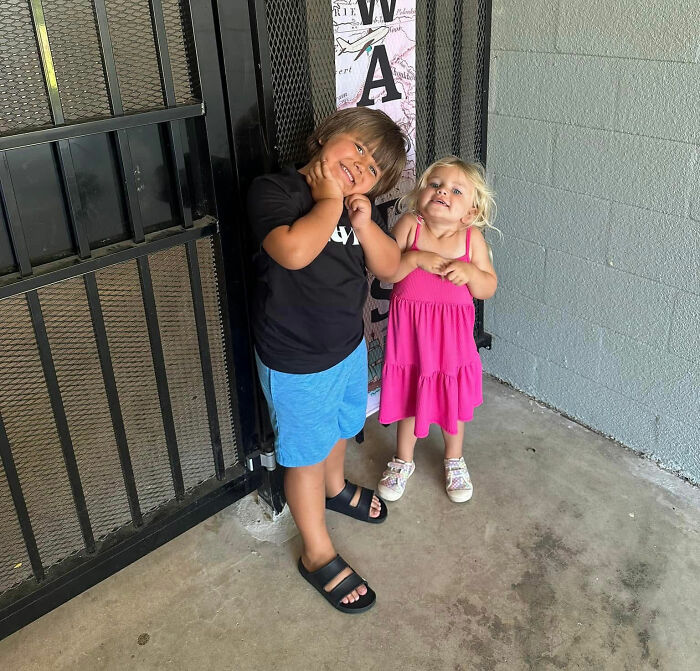 Two young 2 children posing playfully in front of a metal gate.