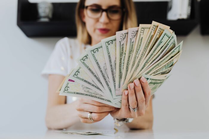 A woman holding a large fan of cash after receiving a life-changing inheritance. A woman holding a large fan of cash after receiving a life-changing inheritance.