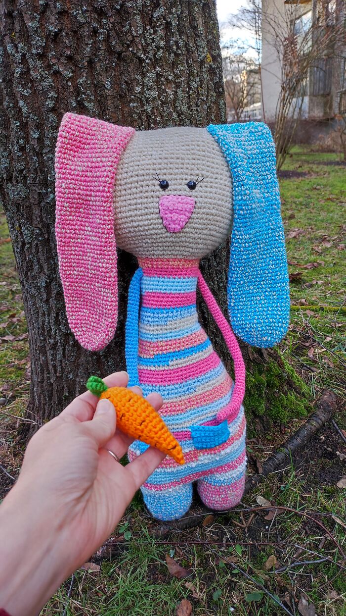 Cute bunny crochet creature next to tree trunk being offered a carrot.