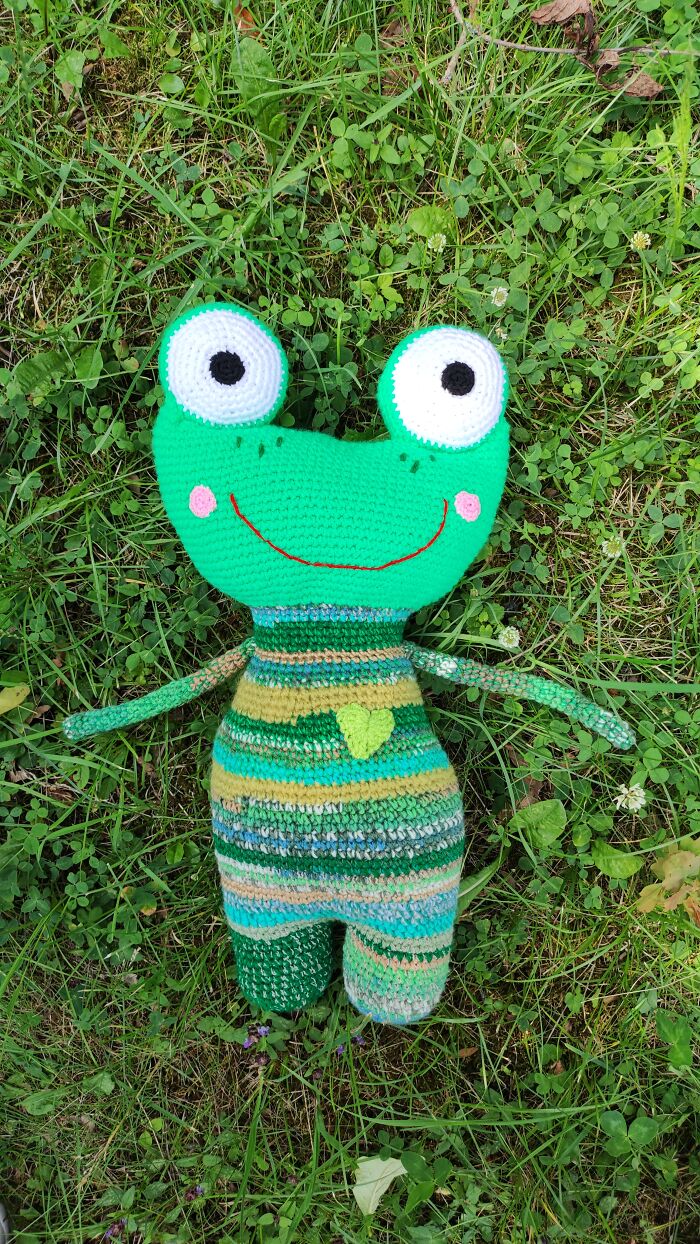 Green frog crochet creature lying on green grass.