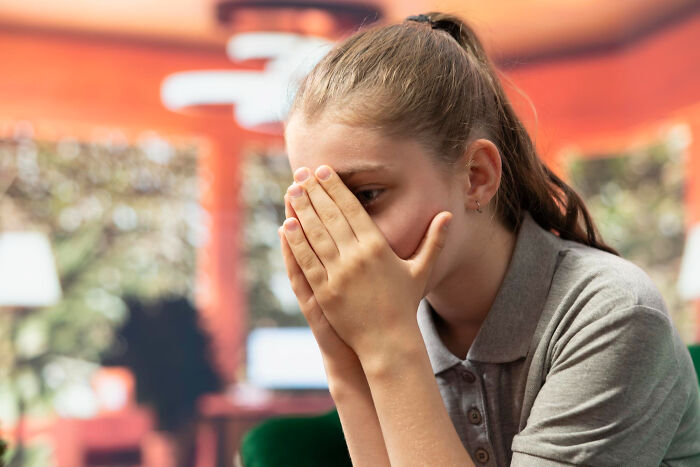 Distressed student covering her face in a classroom, stressed by infuriating teachers.