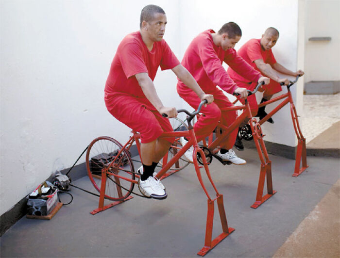 Three men in red uniforms riding stationary bikes connected to power generators, displaying an interesting setup