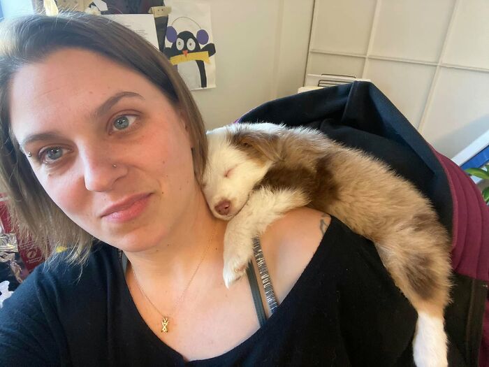 A woman taking a selfie with one of the sleeping puppies resting on her shoulder.