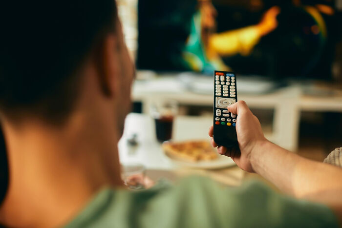 Over the shoulder view of a man holding a TV remote control, connected to personal divorce stories.