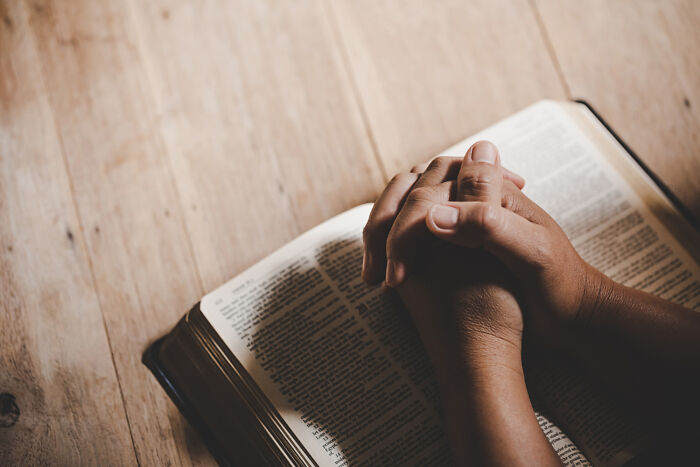 Clasped hands praying over an open book, symbolizing religious beliefs in lesser-known cults.