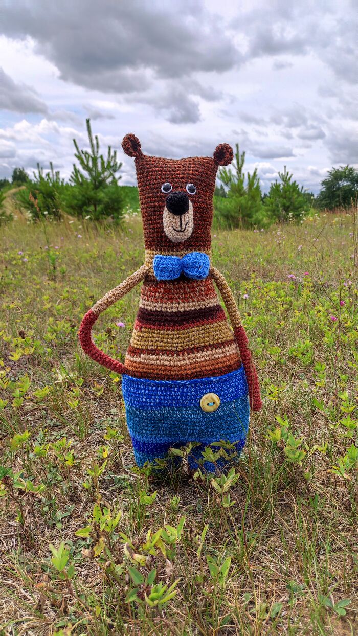 Cute brown bear crochet creature standing in grass field.