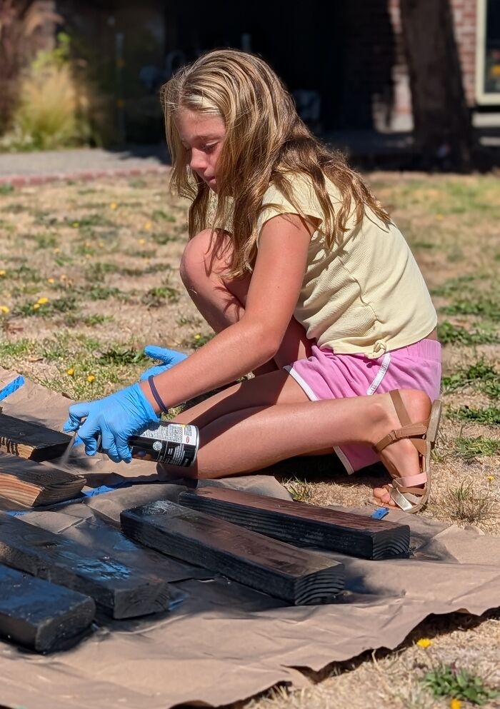 A young girl spray painting wooden boards outdoors using blue safety gloves. A young girl spray painting wooden boards outdoors using blue safety gloves.